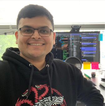 Picture of Raghav Sampangi, with a smiling face, in front of a computer screen.